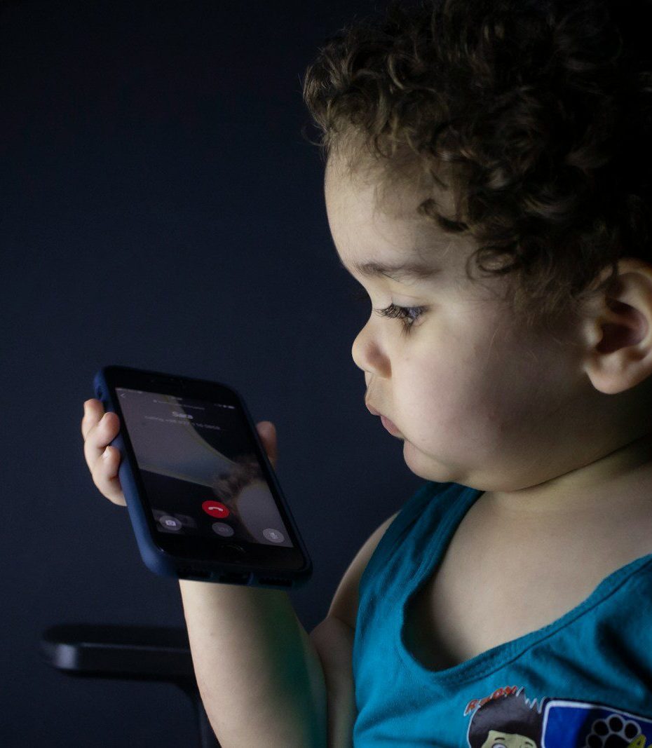 boy in blue tank top holding black smartphone